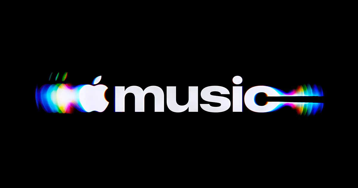 The new Apple Music wordmark in white on black: the Apple symbol and a bold lowercase music, with a blurred rainbow trail streaming off both ends like light bent through liquid.